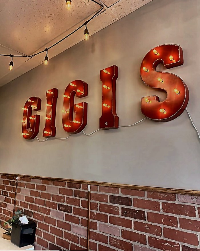 Illuminated GIGI'S marquee letters on the dining room brick wall