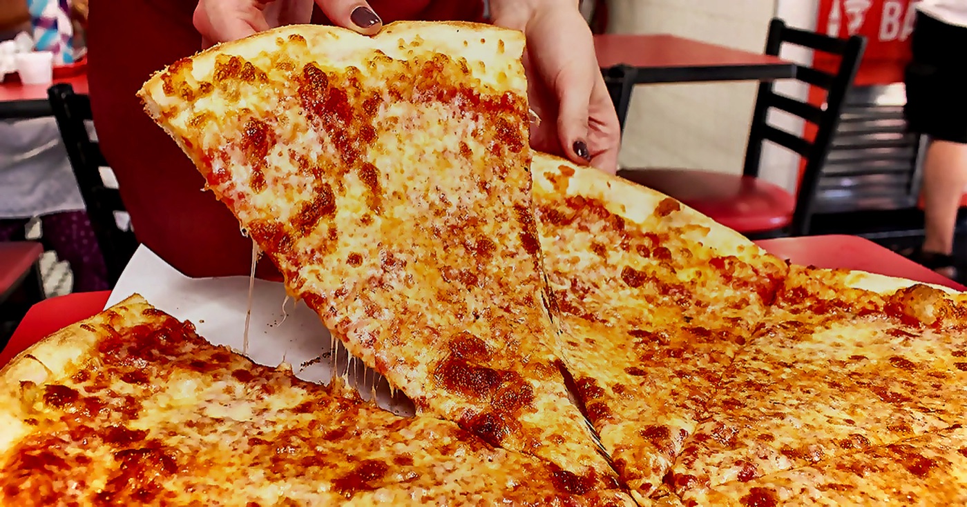 Hand lifting a New York style cheese slice from a whole pie at Gigi's Long Branch