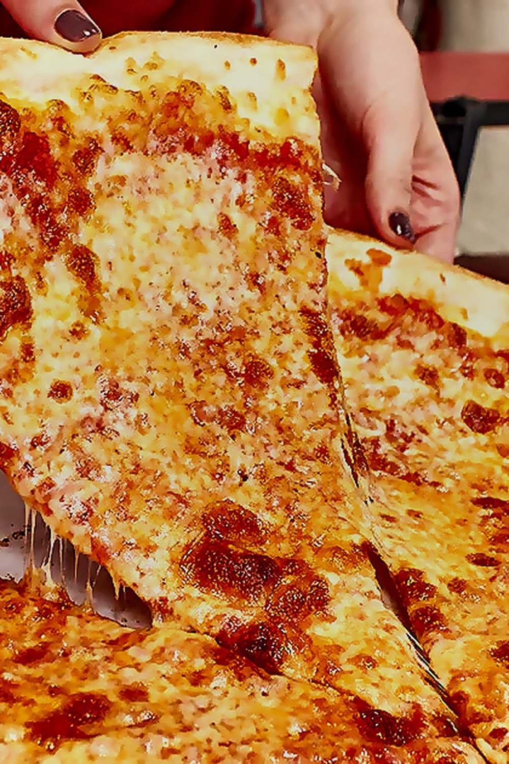 Hand lifting a generous New York style cheese slice from a whole pie at Gigi's Long Branch