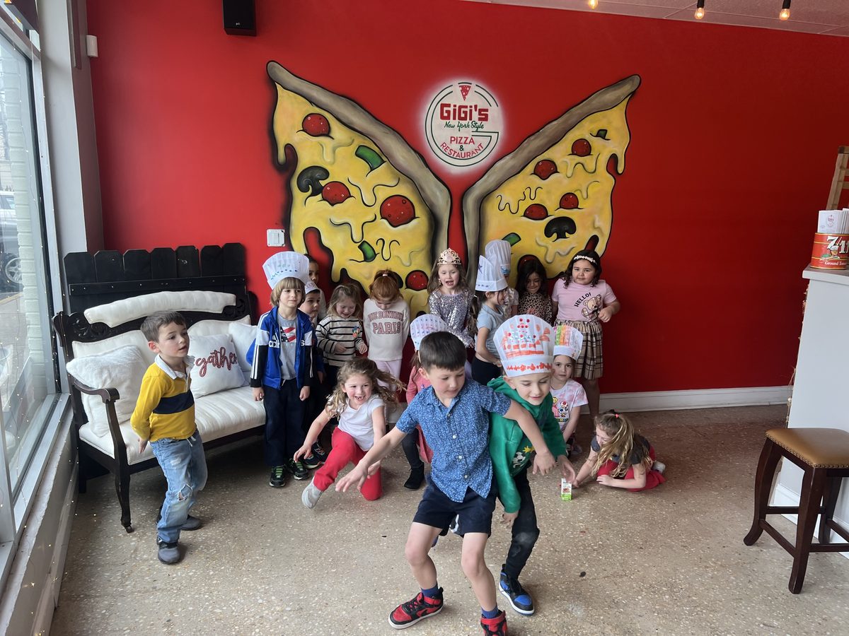 A birthday group in chef hats in front of the painted pizza-wings mural at Gigi's in Long Branch