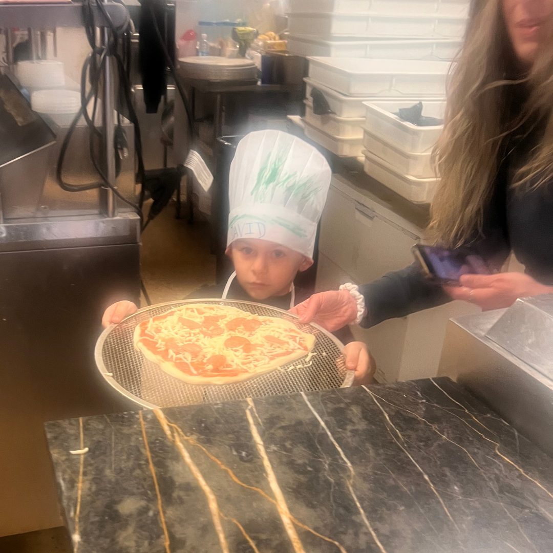 A child in a decorated chef hat proudly holding the pepperoni pizza they made
